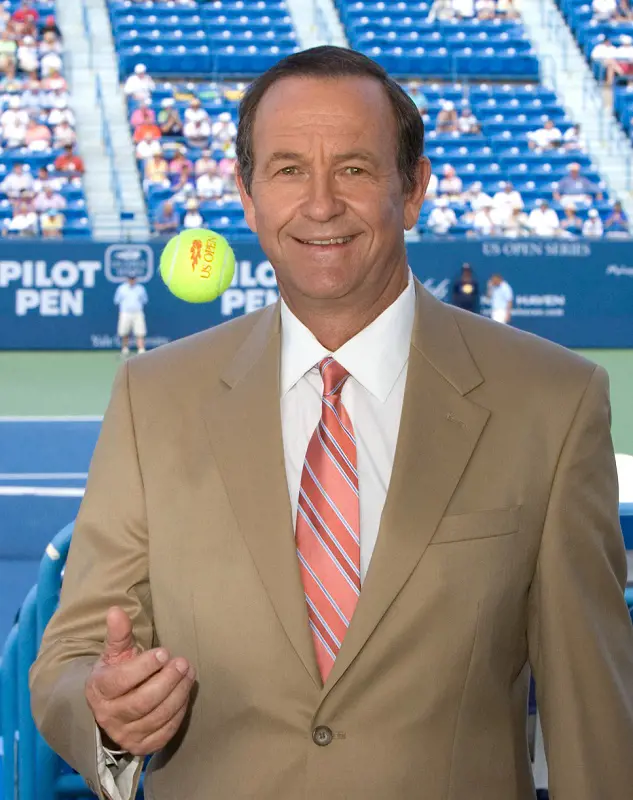 Cliff Drysdale tosses a tennis ball in the air while wearing a suits at the stands of tennis court.