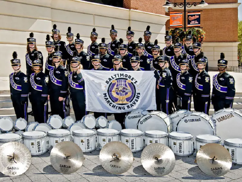 Baltimore' Marching Ravens dressed in their uniform hold their banner and display their instruments.